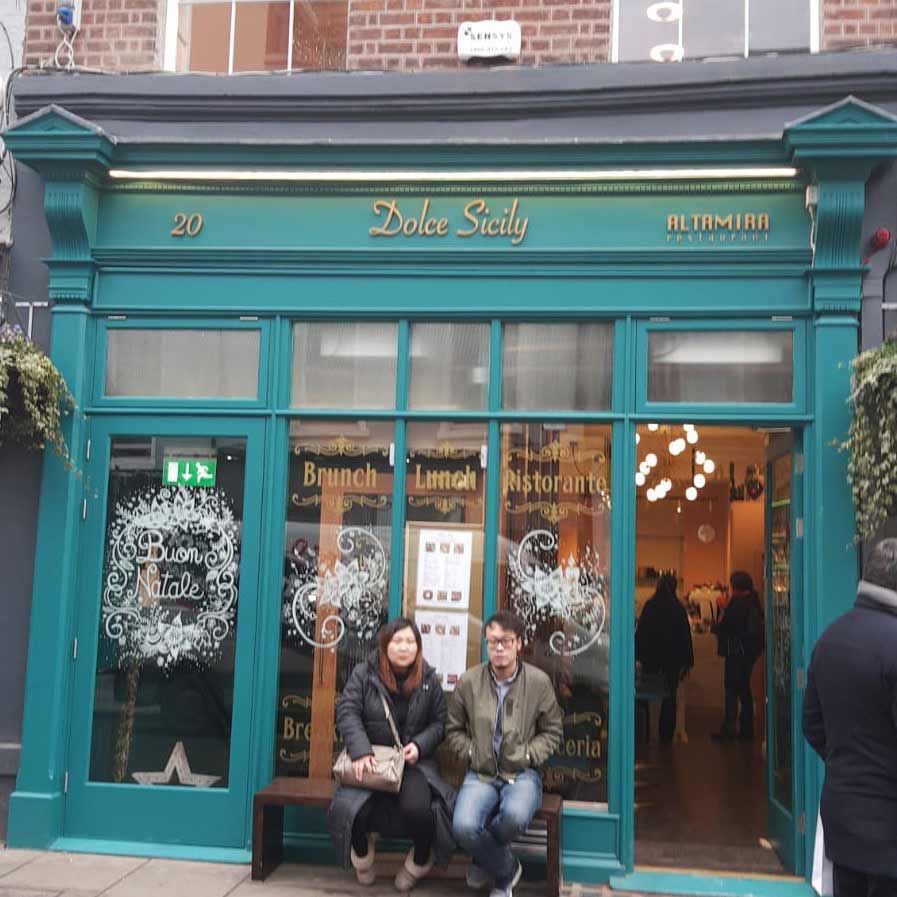 Two tourists sitting in front of Dolce Sicily restaurant - Sensys.ie integrated alarm box above window